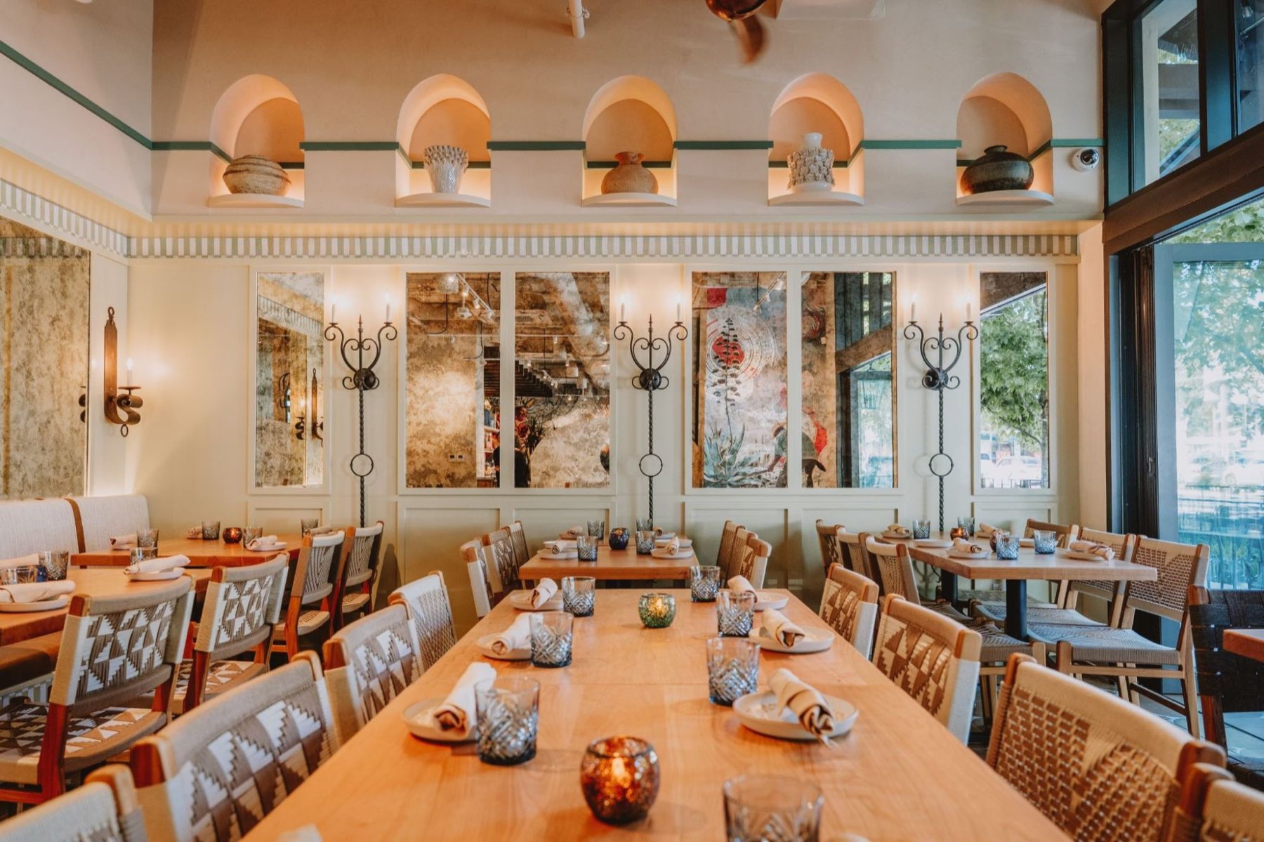 Alisios &mdash; long communal table set beneath arched display niches, wrought-iron candle sconces and tall windows